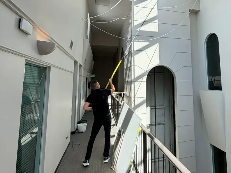 Window cleaner using an extension pole on a skylight above an indoor atrium walkway