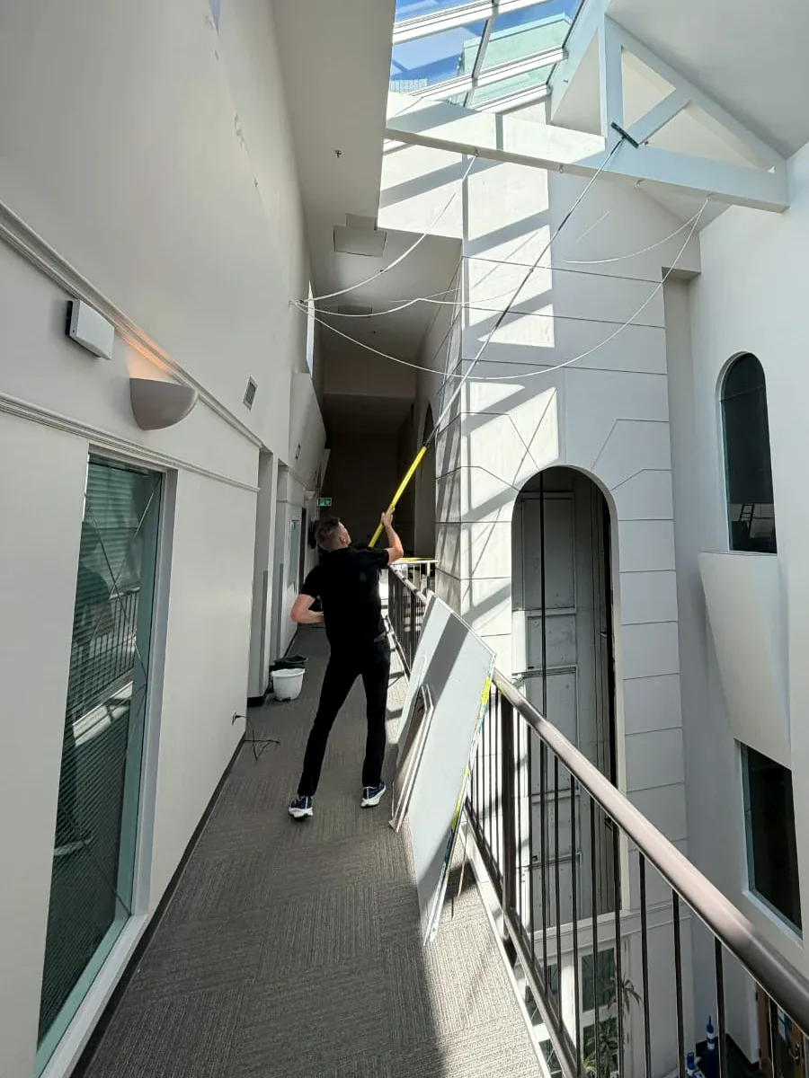 Window cleaner using an extension pole on a skylight above an indoor atrium walkway