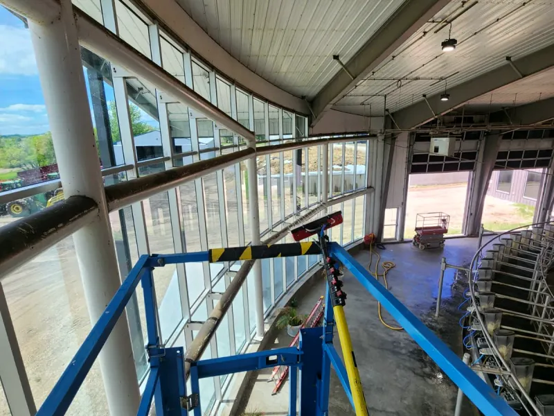 Scissor lift and water-fed pole inside a curved wall of windows in a large agricultural building