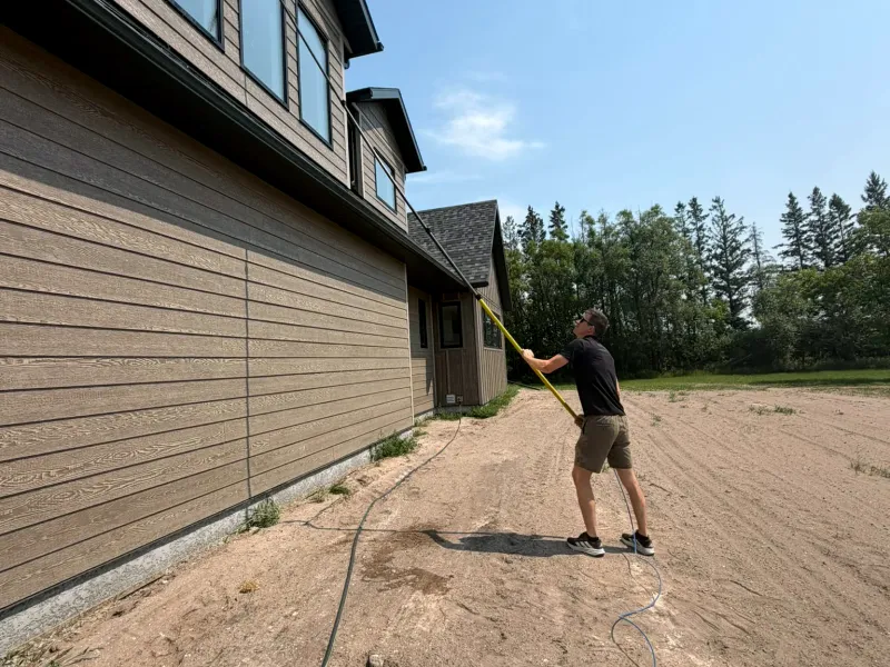 Window cleaner using a water-fed pole to clean second-storey windows on a house with a bare dirt yard