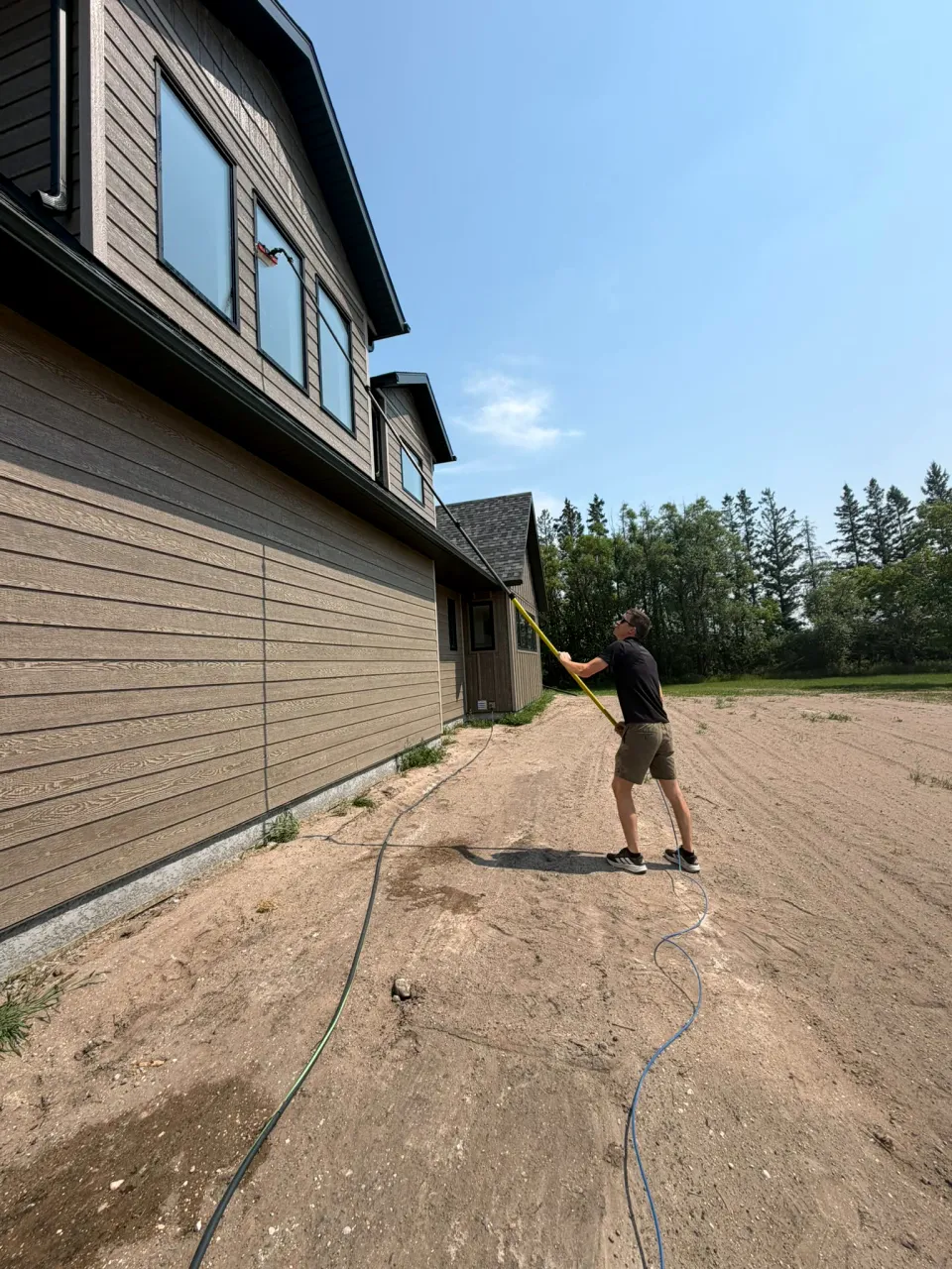 Window cleaner using a water-fed pole to clean second-storey windows on a house with a bare dirt yard