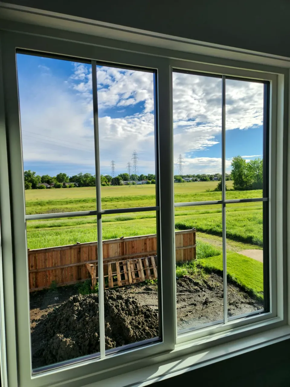 View through a clean double window onto a green field and a freshly graded yard