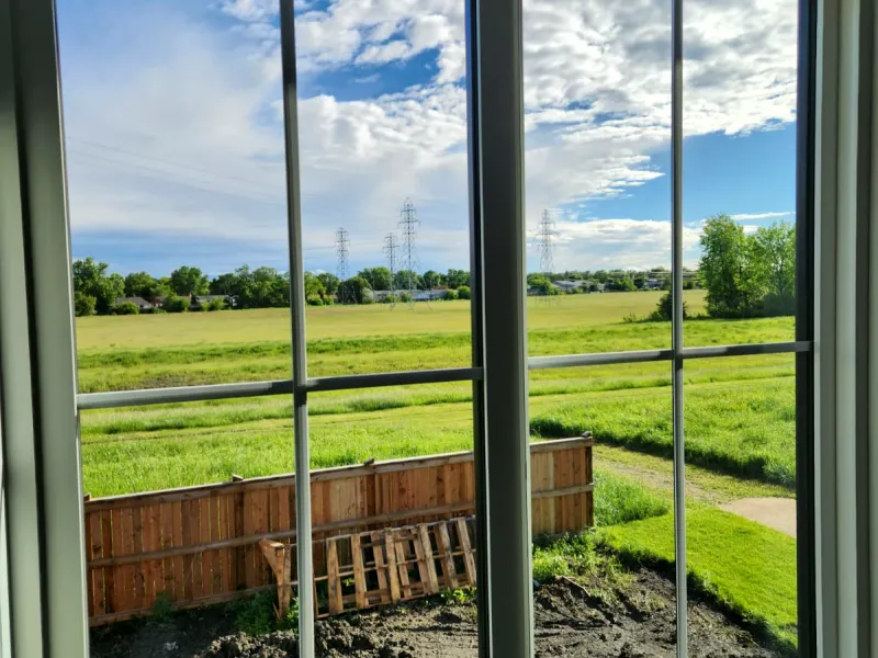 View through a clean double window onto a green field and a freshly graded yard