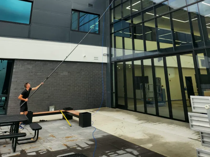 Window cleaner reaching a long water-fed pole up to the second-storey glass of a commercial building